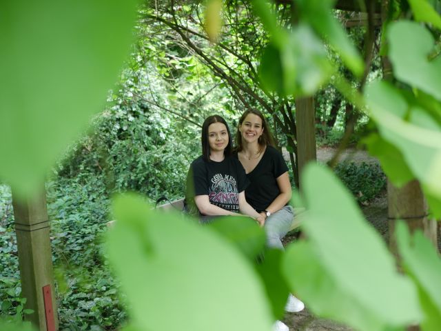 Wyjazd do arboretum Bolestraszyce, dwie dziewczyny w czarnych koszulkach siedzące na ławce, widok spomiędzy liści.