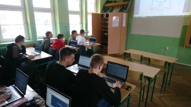 grupa uczniów siedzących przy biurkach przed laptopami