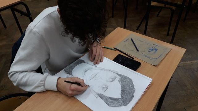 Zbliżenie na ucznia w białej bluzie, który rysuje czyjś portret.