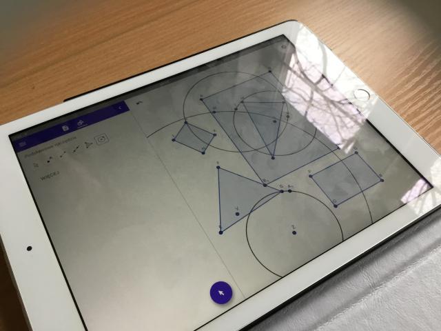 Zbliżenie na tablet, na ekranie przenikające się figury geometryczne.