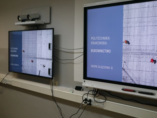 Dwa monitory wiszące na ścianie, na obu widać napis: Politechnika Krakowska, budownictwo, grupa zajęciowa B.