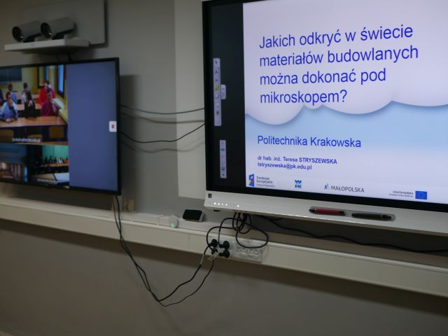 Dwa monitory wiszące na ścianie, na jednym zdjęcie, na drugim napis "jakich odkryć w świecie materiałów budowlanych można dokonać pod mikroskopem?"