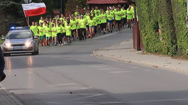 Zdjęcie biegnących uczestników, przed nimi jadące auto policyjne