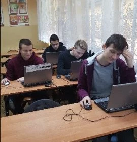 Czterech uczestników kursu siedzących w trzech ławkach przed laptopami.