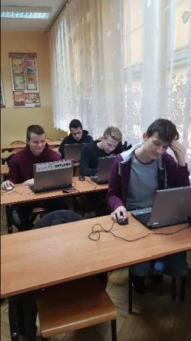 Czterech uczestników kursu siedzących w trzech ławkach przed laptopami.