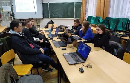 Uczestnicy kursu siedzący po dwóch stronach stołu, między nimi laptopy, w tle ekran rzutnika.